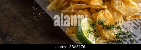 panoramic shot of crunchy potato chips with salt near sliced lime and newspaper on marble surface Stock Photo