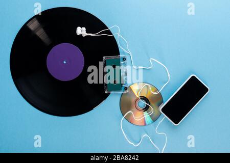 top view of vinyl record, compact disk, earphones, audio tape and smartphone with blank screen on blue, evolution concept Stock Photo