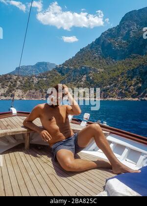 young man relaxing on a wooden boat during a boat trip to Butterfly beach at Fethiye Turkey, Tanning young boy in swim wear Stock Photo