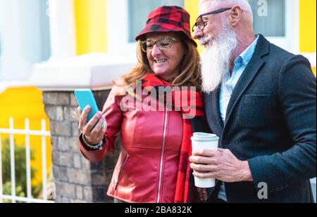 Senior fashion couple using smartphone app in London - Mature people having fun with mobile phone - Travel, love, influencer, technology trends and jo Stock Photo