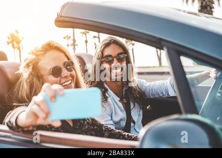 Happy people having fun in convertible car making videos for social network - Young couple enjoyng holiday on cabriolet outdoor - Travel, youth lifest Stock Photo