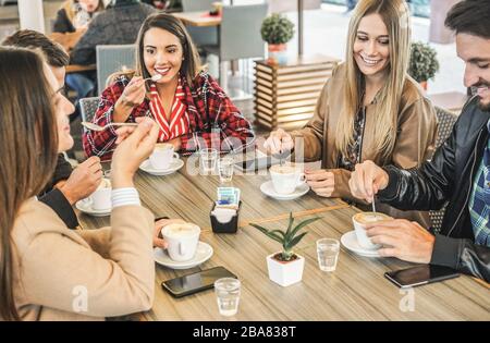 Young friends drinking coffee with milk while doing breakfast in bar bakery shop - Happy people having cappuccino during winter time - Friendship and Stock Photo