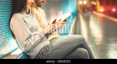 Young couple of friends using mobile phones inside subway train station - Millennials people having fun with technology trends in urban context - Tech Stock Photo