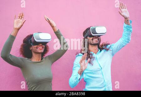 Young couple having fun with virtual reality goggles headset glasses -  Happy people playing game with new trends technology - Future concept - Focus Stock Photo