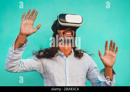 Young man using virtual reality headset with blue wall in background - Trendy guy having fun with new trend technology - Tech, fun and future concept Stock Photo