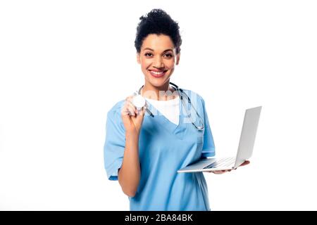 African american nurse showing stethoscope and holding laptop smiling and looking at camera isolated on white Stock Photo
