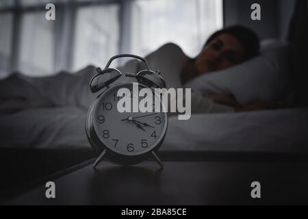 selective focus of alarm clock on bedside table near awake woman Stock Photo