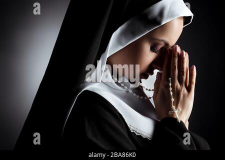 beautiful young nun praying with cross on grey Stock Photo