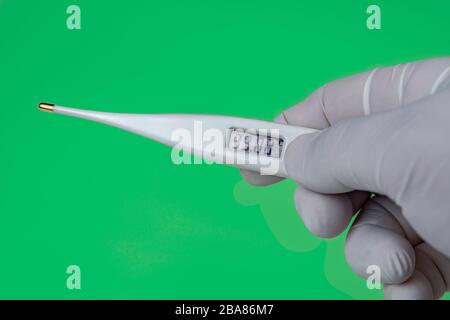 Hand with a Thermometer on Green background. The thermometer shows a temperature of 39 Celsius. Coronavirus 2019-nCoV. Corona virus outbreaking. Stock Photo