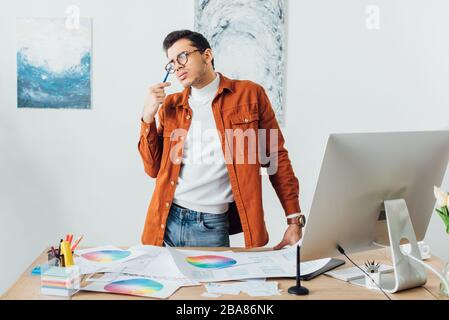 Dreamy designer looking away near website design templates, color circles and computer on table Stock Photo
