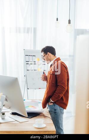 Side view of designer holding marker near website sketches,color circles and computer on table on table Stock Photo