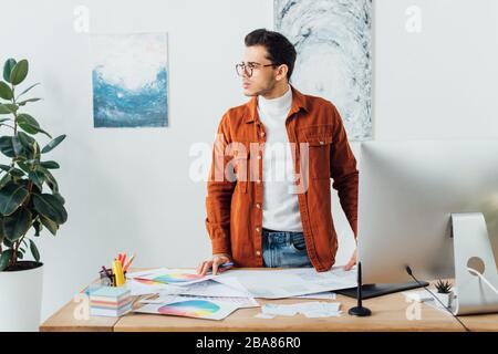 Designer looking away near gadgets, color circles and layouts of user experience design on table Stock Photo