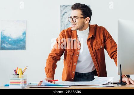 Handsome ux designer smiling while working with templates near computer at table in office Stock Photo