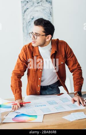 Handsome ux designer looking away while working with website templates on table Stock Photo