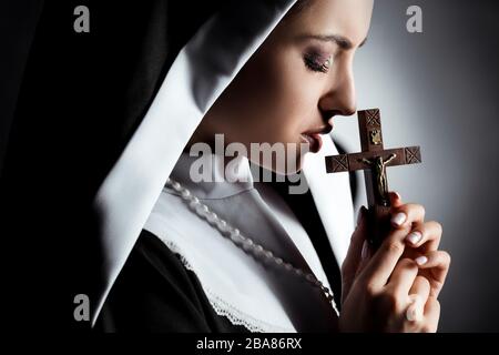 sad young nun praying with cross on grey Stock Photo