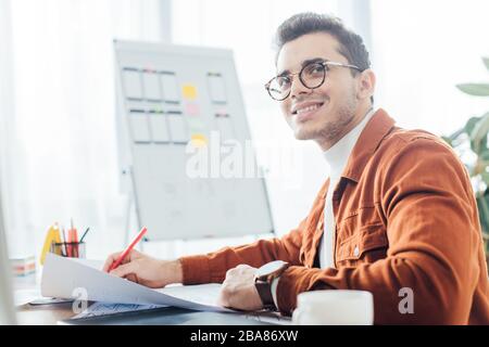 Side view of smiling ux designer holding marker while working with website templates at table Stock Photo