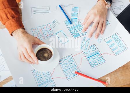 Cropped view of developer working with ux website templates and holding coffee cup on table Stock Photo