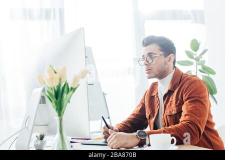 Side view of ux designer working with computer and graphics tablet on table in office Stock Photo