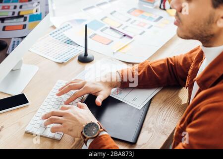 Cropped view of developer using computer near layouts of ux design on table Stock Photo