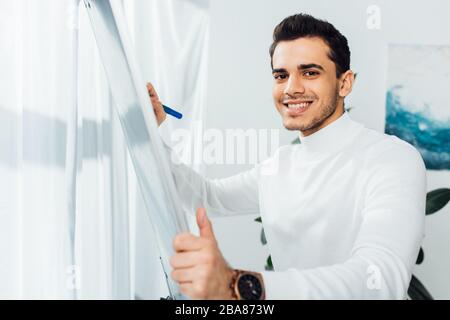 Smiling designer looking at camera while using whiteboard in office Stock Photo