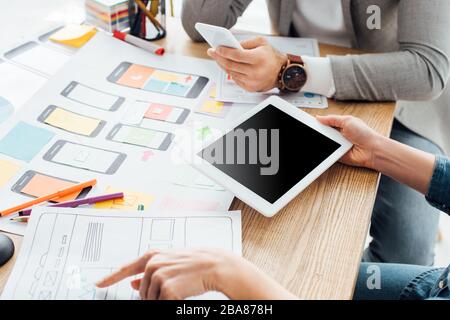 Cropped view of ux designers using gadgets near mobile frameworks on table isolated on grey Stock Photo