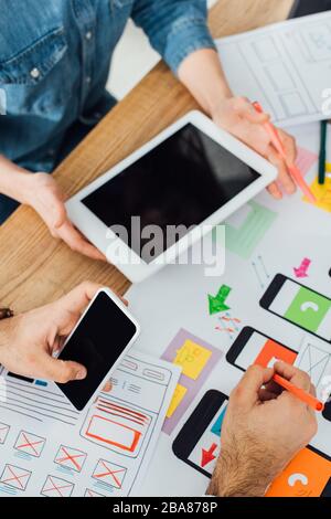 Selective focus of ux designers using smartphone and digital tablet near mobile frameworks on table isolated on grey Stock Photo