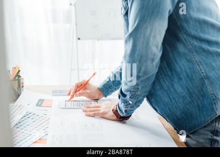 Cropped view of ux designer working with sketches of mobile interface and color palettes on table Stock Photo