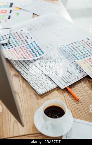 Selective focus of coffee cup and computer monitor near color palettes and sketches of ux design on wooden table Stock Photo