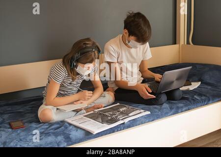 Children a boy and a girl in a medical mask carry out lessons through a laptop. Online education during a pandemic epidemic. The concept of home isola Stock Photo