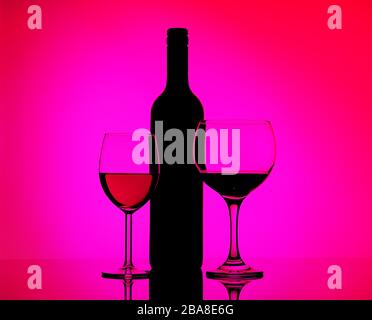 Two filled glasses with red wine and sherry, black silhouette of bottle on a mirrored background in side pink and purple lighting. Concept sales, disc Stock Photo