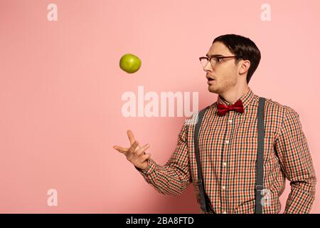 shocked male nerd in eyeglasses throwing apple on pink Stock Photo