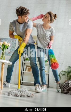 selective focus of cheerful girl and man looking at each other while cleaning in living room Stock Photo