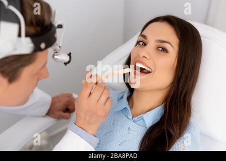attractive woman looking at camera while ent physician holding tongue depressor Stock Photo