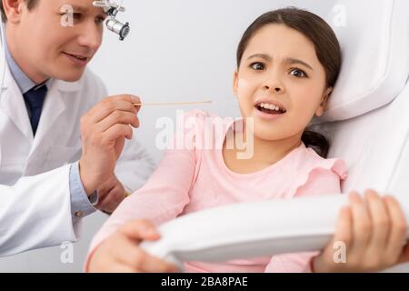 smiling ent physician holding tongue depressor near scared child Stock Photo