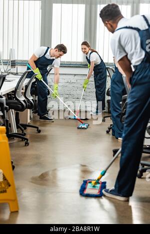 multicultural team of young cleaners washing floor with mops in office Stock Photo