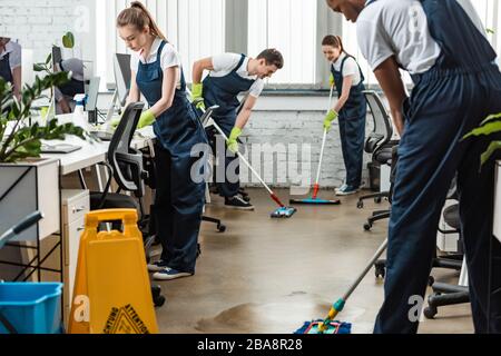 multicultural team of young cleaners washing floor with mops in office Stock Photo