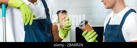 partial view of multicultural cleaners holding coffee to go in office, panoramic shot Stock Photo