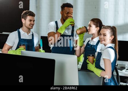 happy multicultural cleaners drinking coffee to go in office Stock Photo