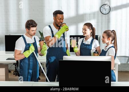 cheerful multicultural cleaners drinking coffee to go in office Stock Photo