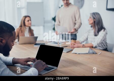 selective focus of african american man using laptop and his colleagues talking on background Stock Photo