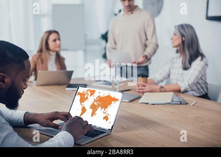 selective focus of african american man using laptop with map and his colleagues talking on background Stock Photo