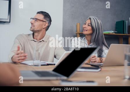 selective focus of smiling multicultural colleagues looking away Stock Photo