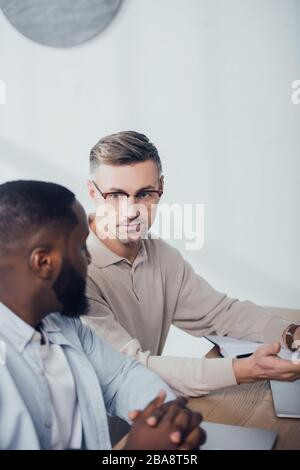 multicultural colleagues talking and sitting at table in creative agency Stock Photo