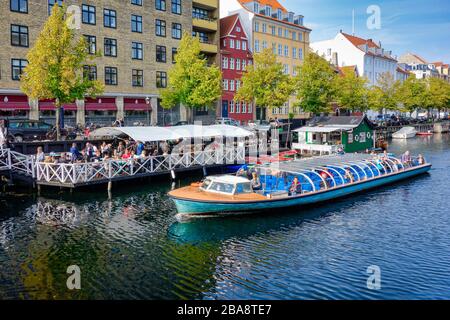 Christianshavn Canal in Copenhagen Denmark with restaurant & vessels along both quays and harbour cruise vessel passing through Stock Photo
