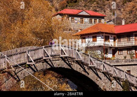 Lonely woman crossing the old stone bridge over Aoos river at Vovoussa village, Zagori region, Ioannina, Epirus, Greece. Stock Photo