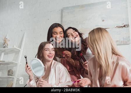 Multiethnic women doing hairstyle, manicure and laughing at bachelorette party Stock Photo