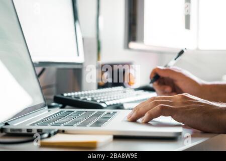Person holding a pen working from home at their desk with computers Stock Photo