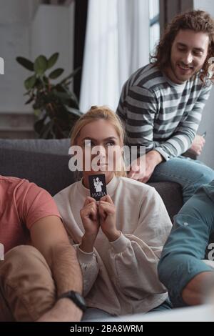 KYIV, UKRAINE - JANUARY 27, 2020: smiling girl holding card while playing mafia game with friends Stock Photo