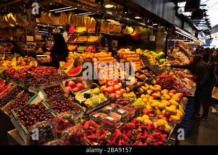 La Boqueria food market in Barcelona, Spain, colourful fruits and vegetables, seafood, lobsters, hamon, jamón serrano / ibérico (spanish ham) hanging Stock Photo