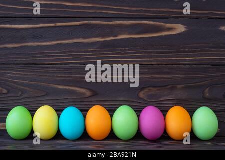 Painted colorful Easter eggs on dark wooden boards. Paschal template with text space. Holiday greeting card in laconic style Stock Photo